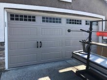 Amarr double garage door in Sandtone with grooved carriage-house panels, grid windows and black handles