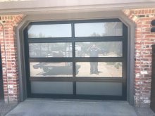 Black aluminum full-view garage door with frosted glass in an angled-corner opening between red brick columns