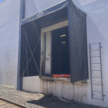 Finished retractable rail shelter at a warehouse opening beside railroad tracks in Modesto