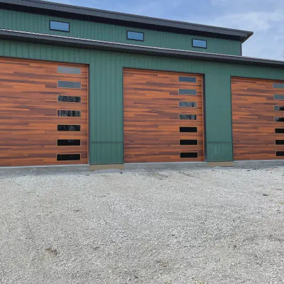 Three cedar-tone CHI Planks garage doors with vertical window stacks on a green metal building