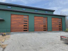 Three cedar-tone CHI Planks garage doors with vertical window stacks on a green metal building