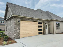 Natural oak CHI Planks garage door with vertically stacked windows on a brick home