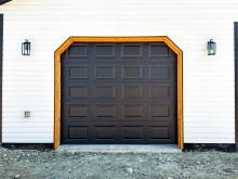Black short raised panel garage door with wood-trimmed opening on a white building