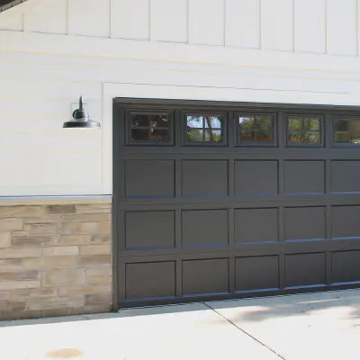 Black CHI recessed short-panel garage door with top-row windows on a white farmhouse-style exterior