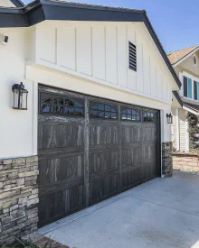 Carbon oak CHI Stamped Carriage House garage door with arched windows on a white home