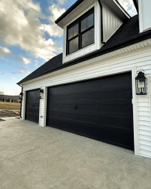 Black C.H.I. stamped carriage house garage doors with decorative handles on a white farmhouse