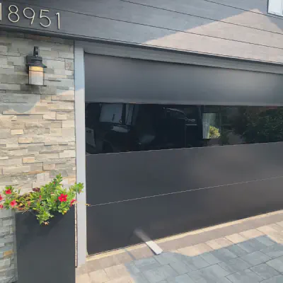 Black CHI Sterling garage door with a horizontal band of dark glass on a stone home