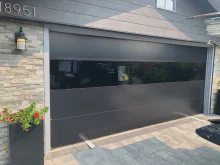 Black CHI Sterling garage door with a horizontal band of dark glass on a stone home